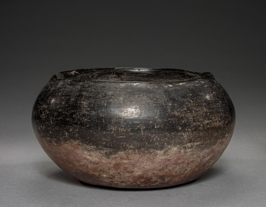 Rounded Predynastic Egyptian bowl with a dark upper surface fading into reddish brown toward its base.